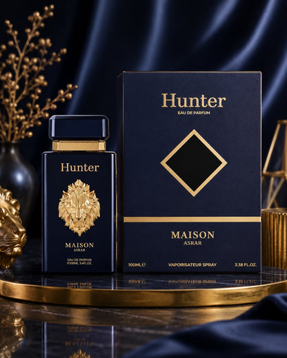 Noor Fragrances Hunter Maison Asrar Eau de Parfum bottle and box with gold lion emblem on a dark reflective surface.